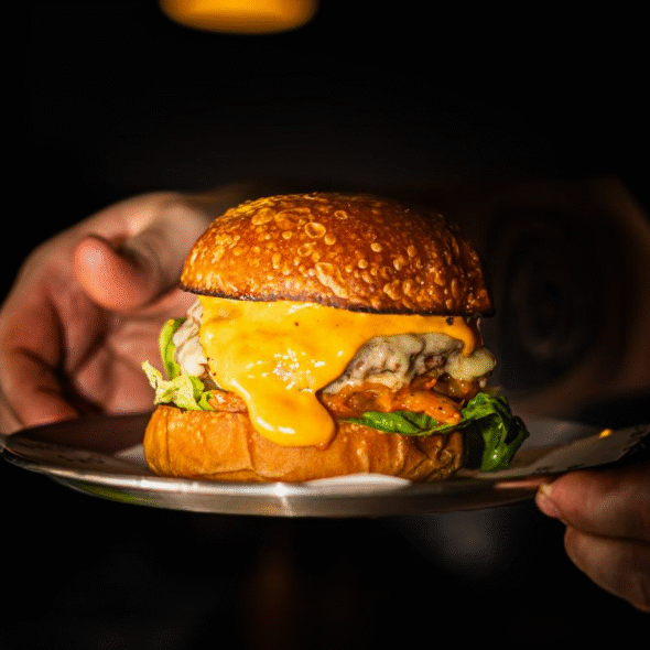 A hand gripping a juicy burger topped with cheese, representing Burger Shop Hereford London.