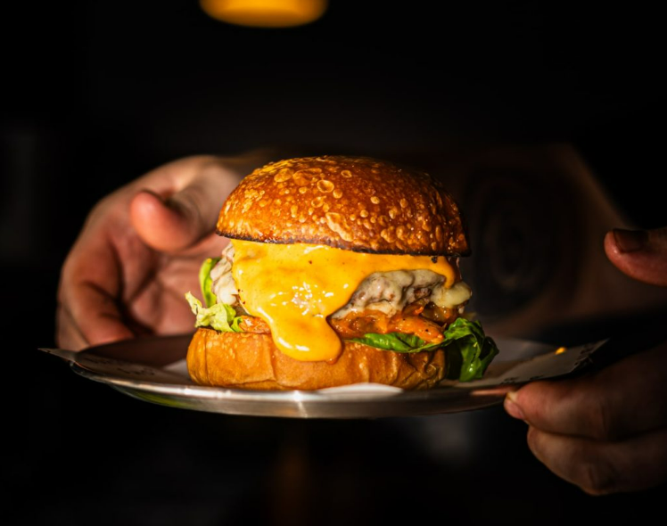 A hand gripping a juicy burger topped with cheese, representing Burger Shop Hereford London.